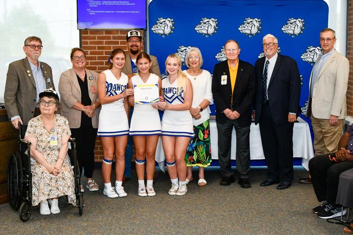 A group of cheerleaders in uniform with school board members, smiling and holding an award