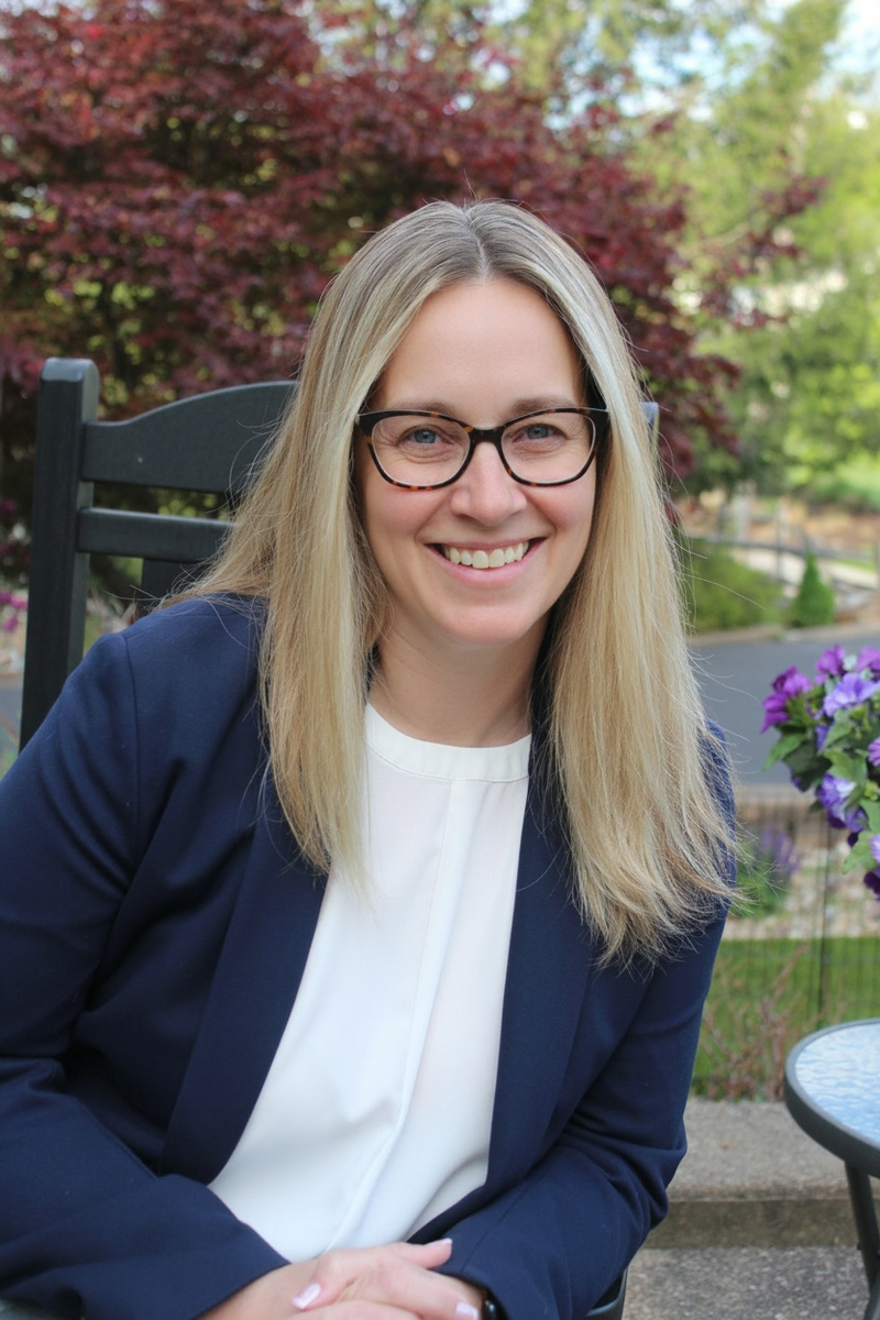 blonde straight haired woman with glasses in blazer near flowers