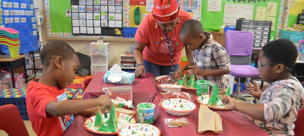 adult assistant helps three boys decorate green frosted ice cream cones with candies