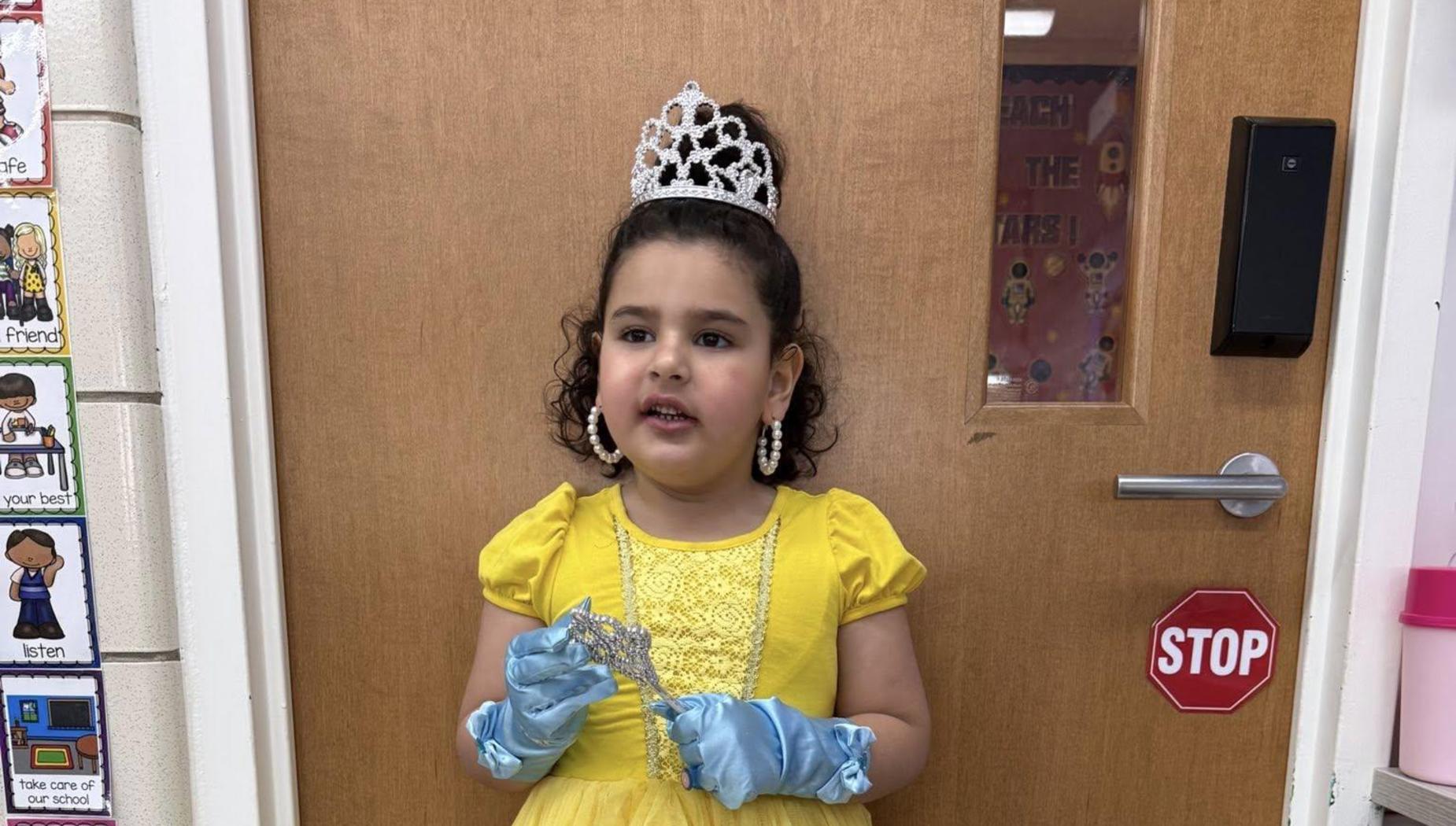 Girl in a yellow dress holding a sparkling wand by a wooden door.