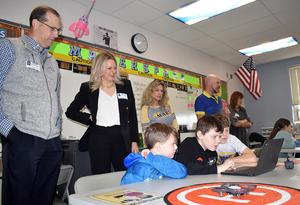 Three adults watching three students using a laptop to fly a drone.