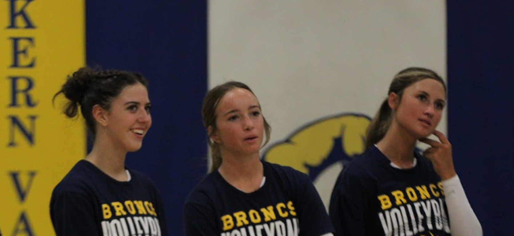 Three volleyball players in team t-shirts chatting on the court.