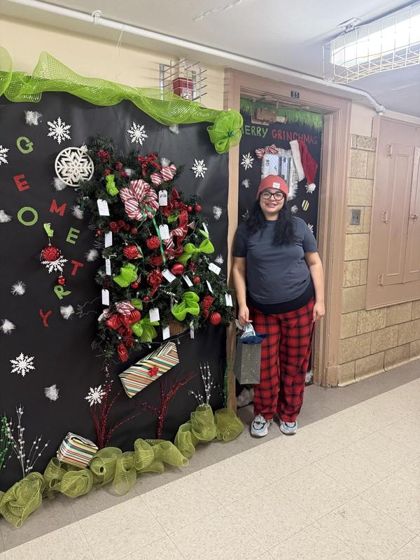 Ms. Chavez beside her decorated door. The all and door outside of her classroom is decorated in festive imagery.