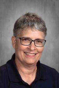 Smiling woman with short gray hair wearing glasses and a plaid shirt.
