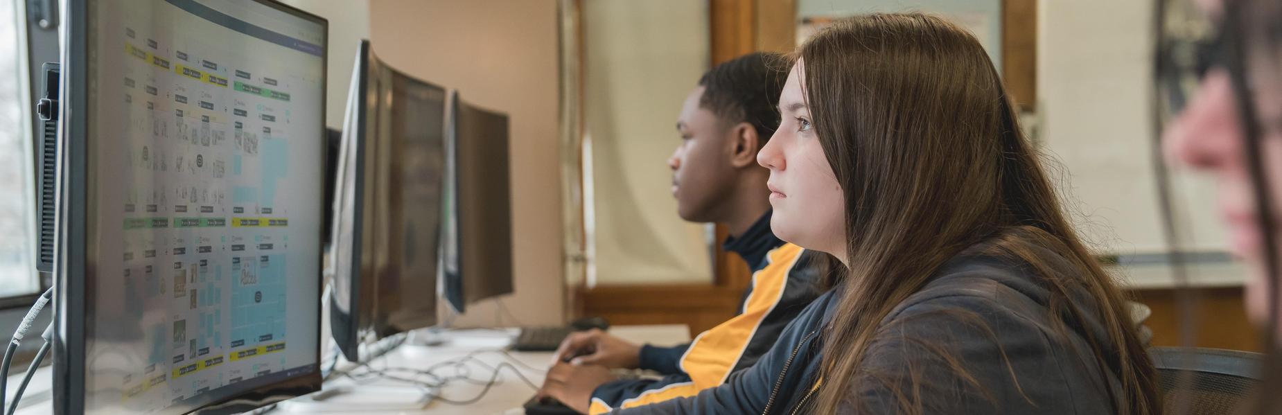 Close-up of students working on computers, focused on screens at a technology station.