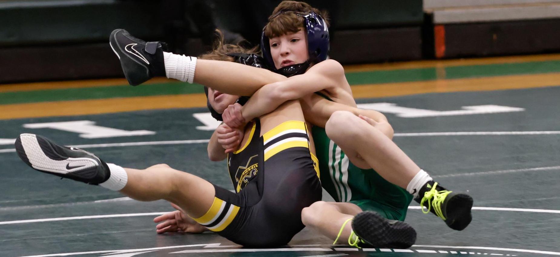 Two young wrestlers engaged in a match on a green wrestling mat.