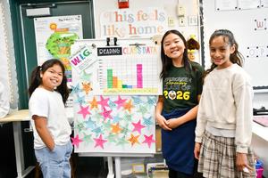 Three students stand beside a poster board displaying their classroom work.