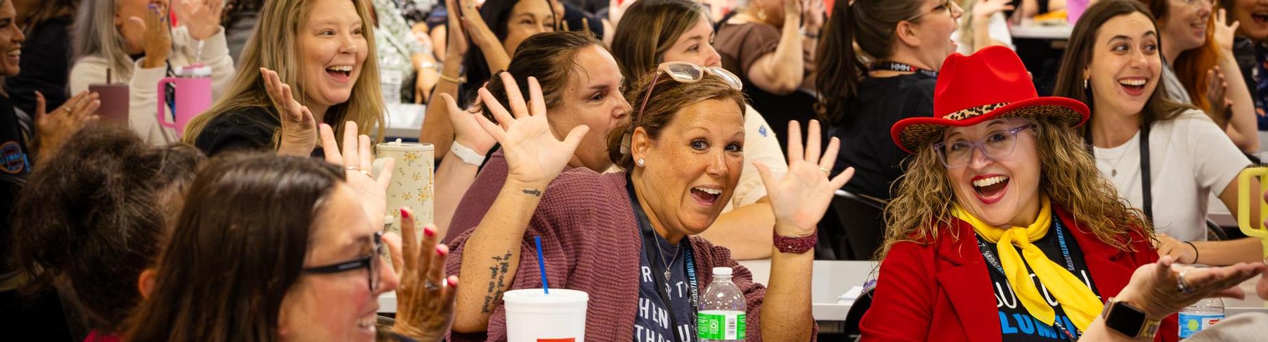 A large group of people smiling and waving enthusiastically in a lively setting.