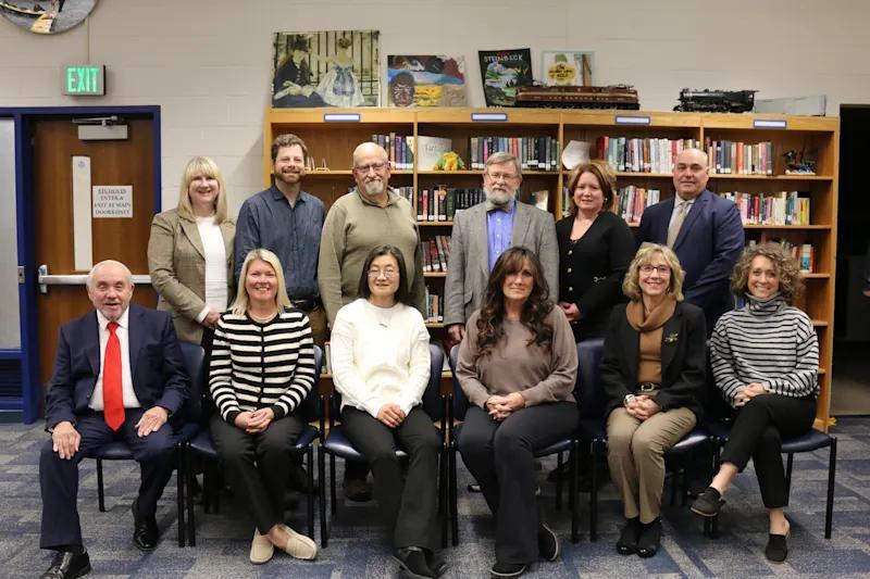 Group portrait of twelve people seated and standing in a library setting.