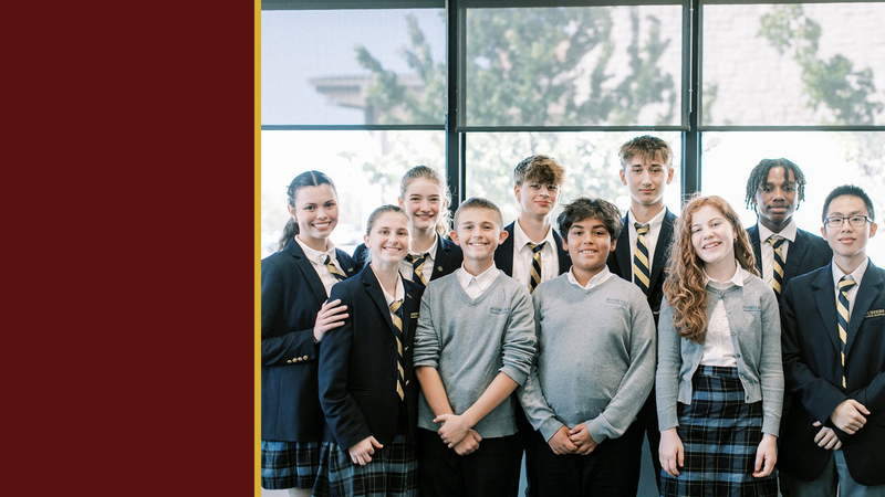 Smiling students in uniform stand together by large windows