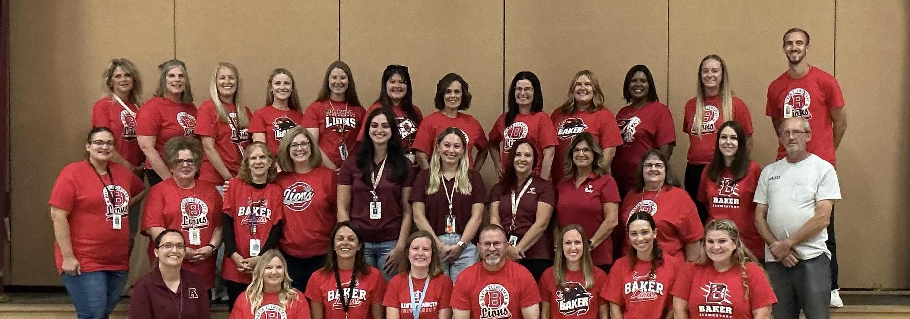 Group of educators posing together in red and maroon shirts, smiling at the camera.
