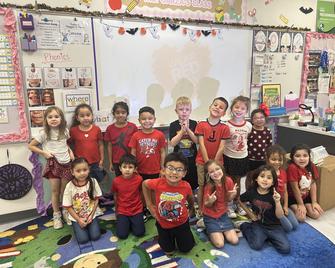 Group of children in red shirts posing for a photo in a classroom.