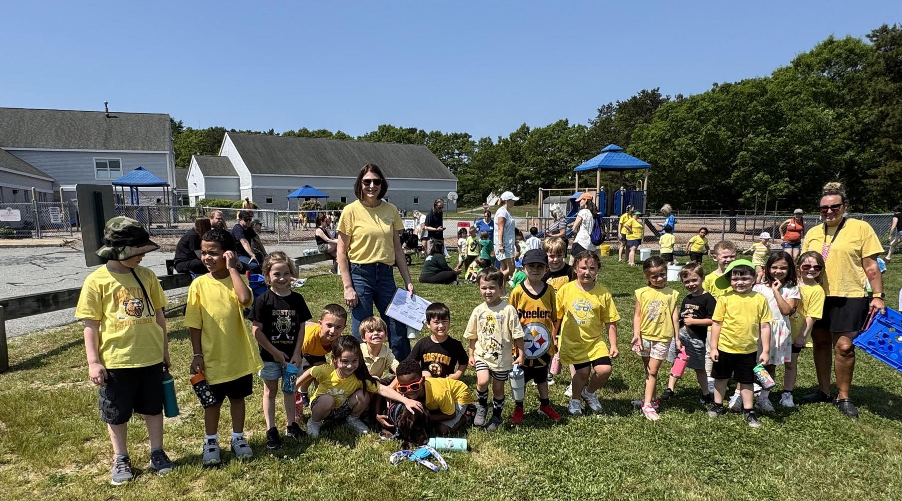 A group of children and adults gathered outdoors, all wearing yellow shirts.