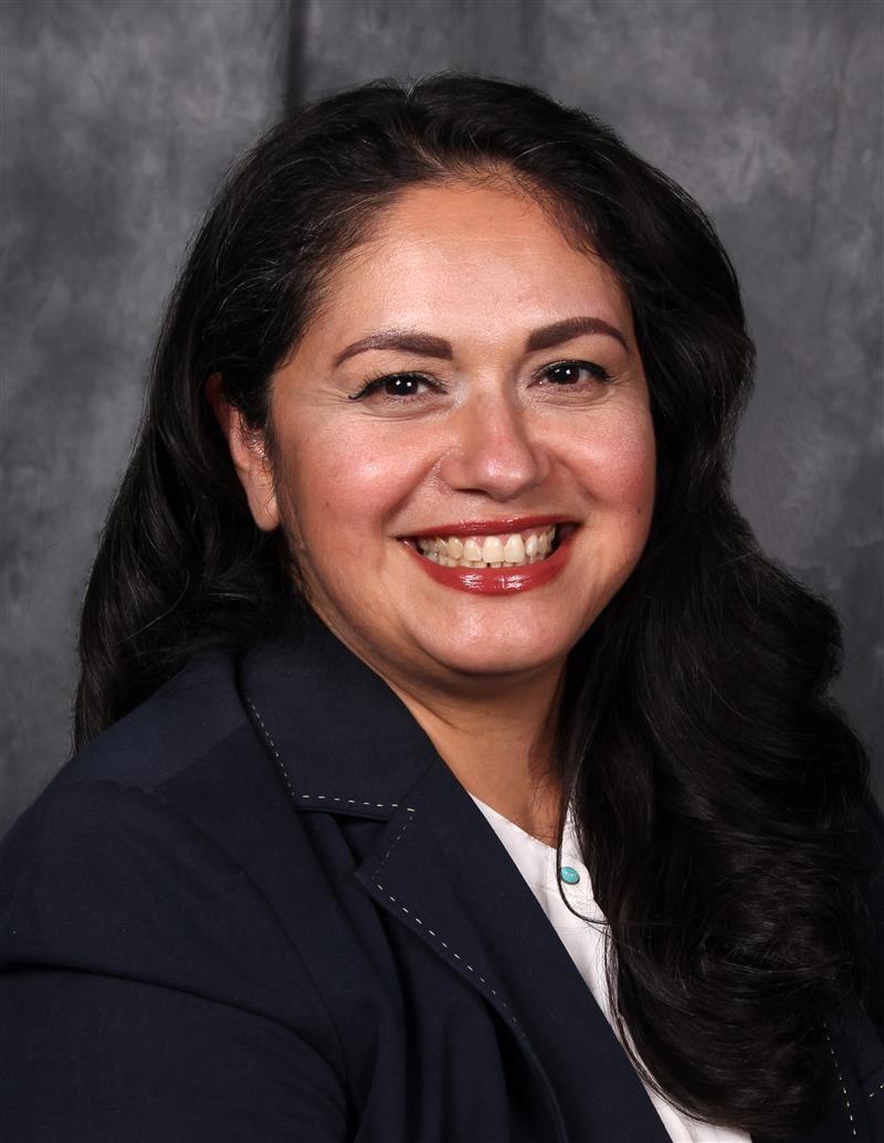 Amy Bustos wearing a navy blazer in front of a textured gray backdrop.