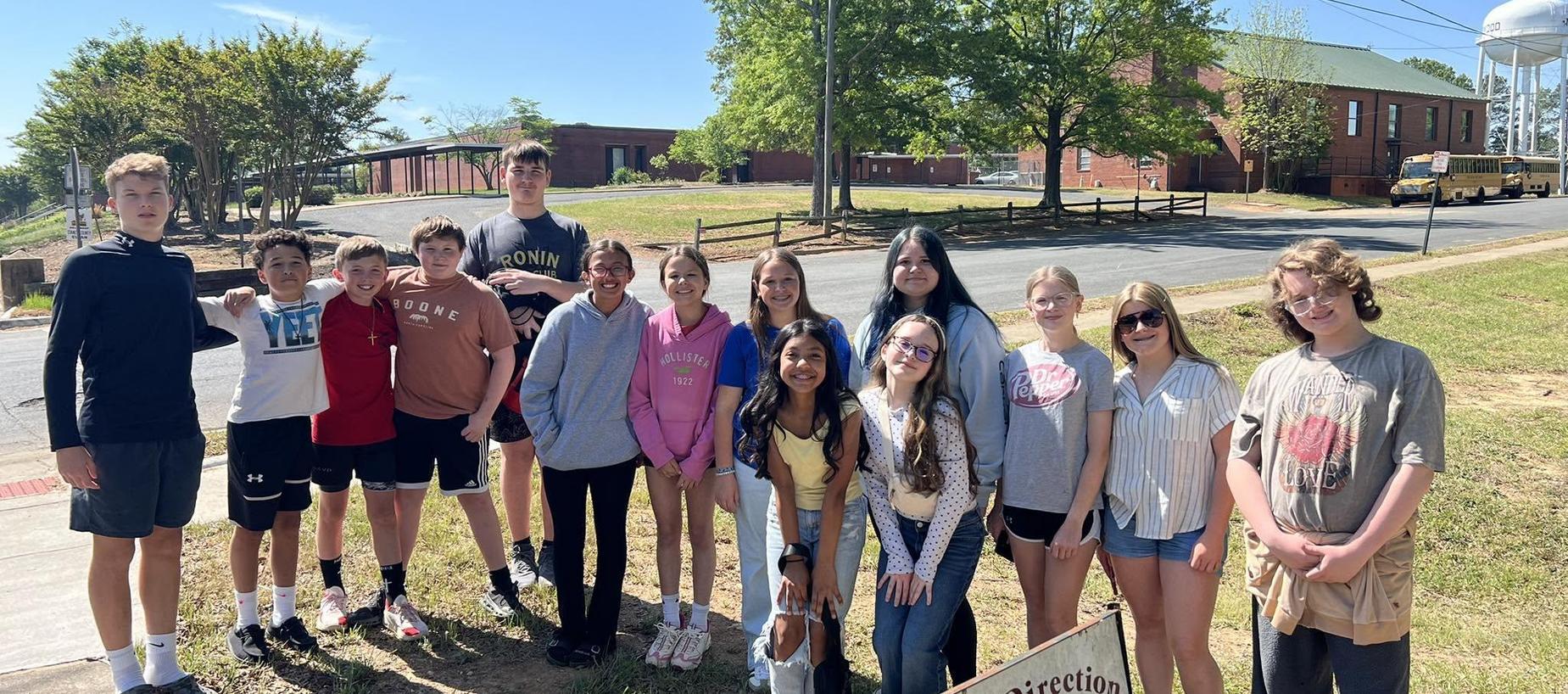 Group of children and teens posing together outdoors with trees and buildings in the background.