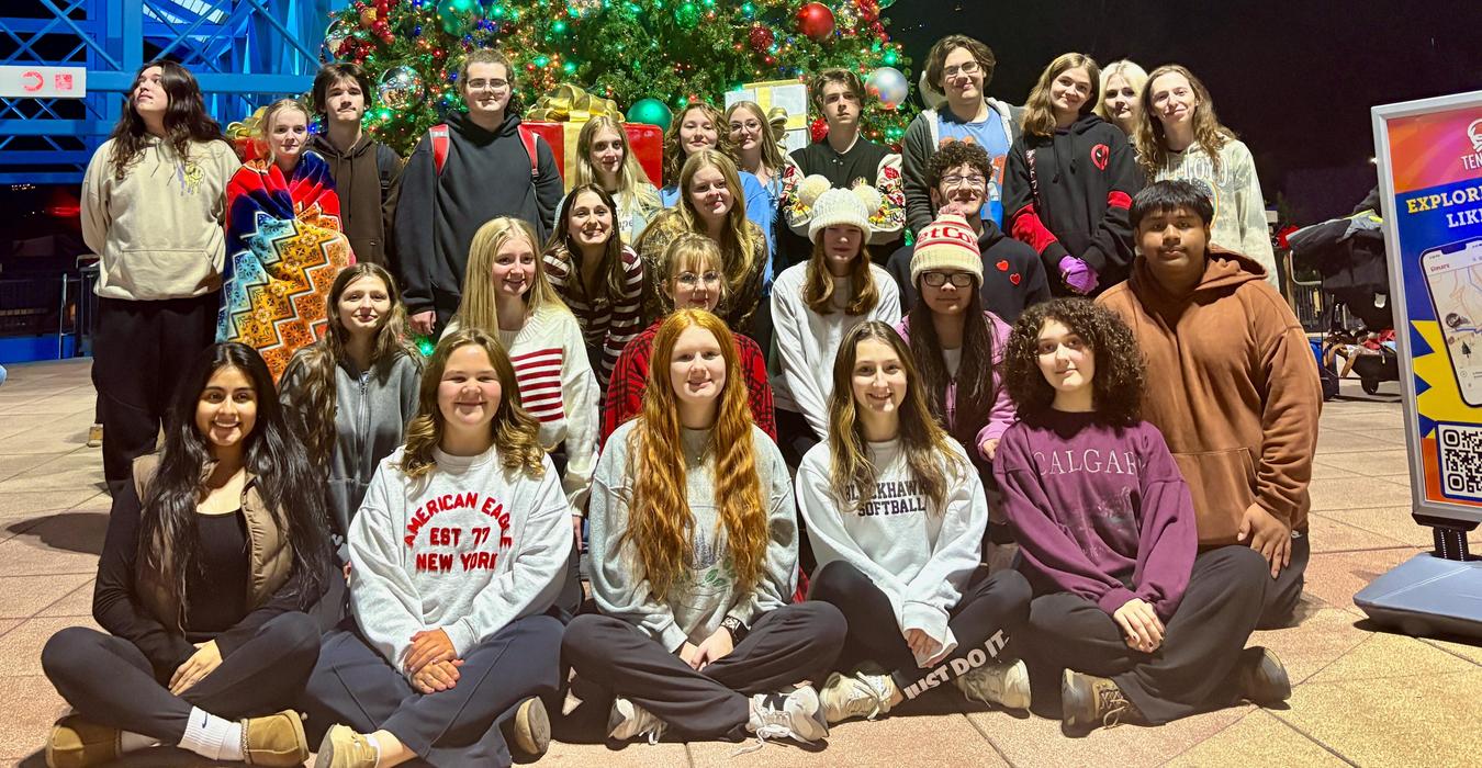 A large group of people posing together in front of a decorated Christmas tree at night.