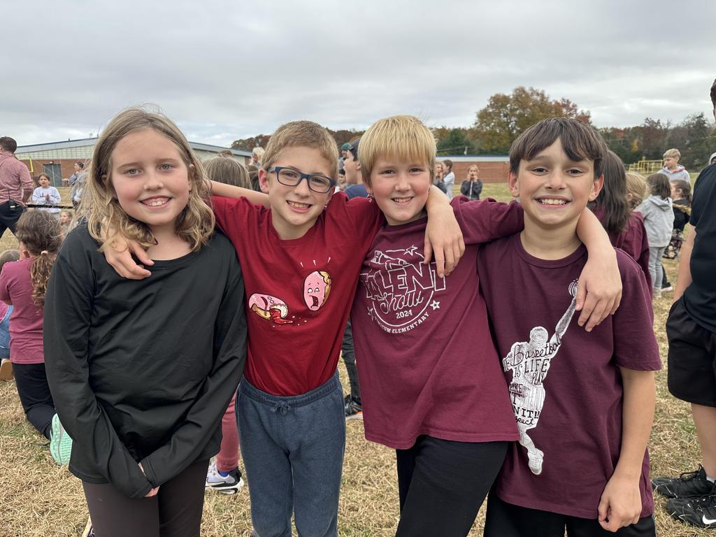 Four students on the playground posing with their arms around each other's shoulders.