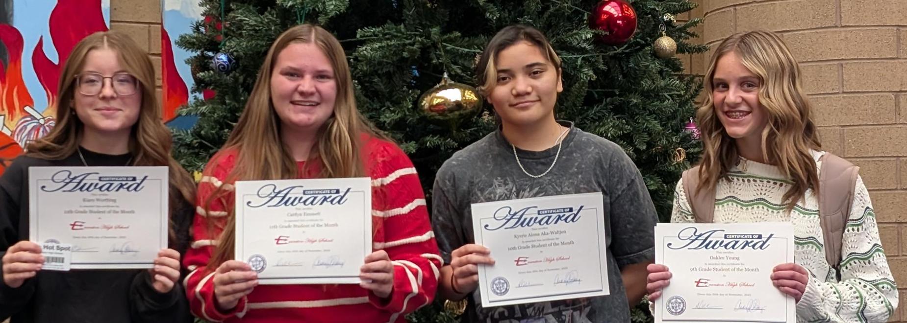 Four female students with award certificates standing by a Christmas tree.