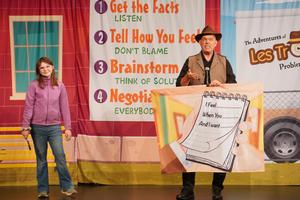 A student stands beside the performer who has sign about sharing feelings.