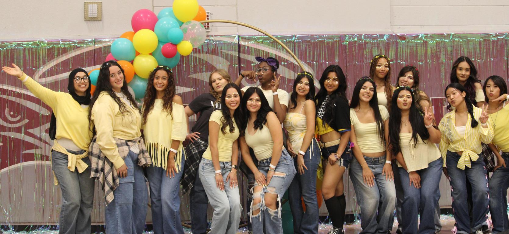 Group of young women in matching yellow outfits posing together in a festive setting.