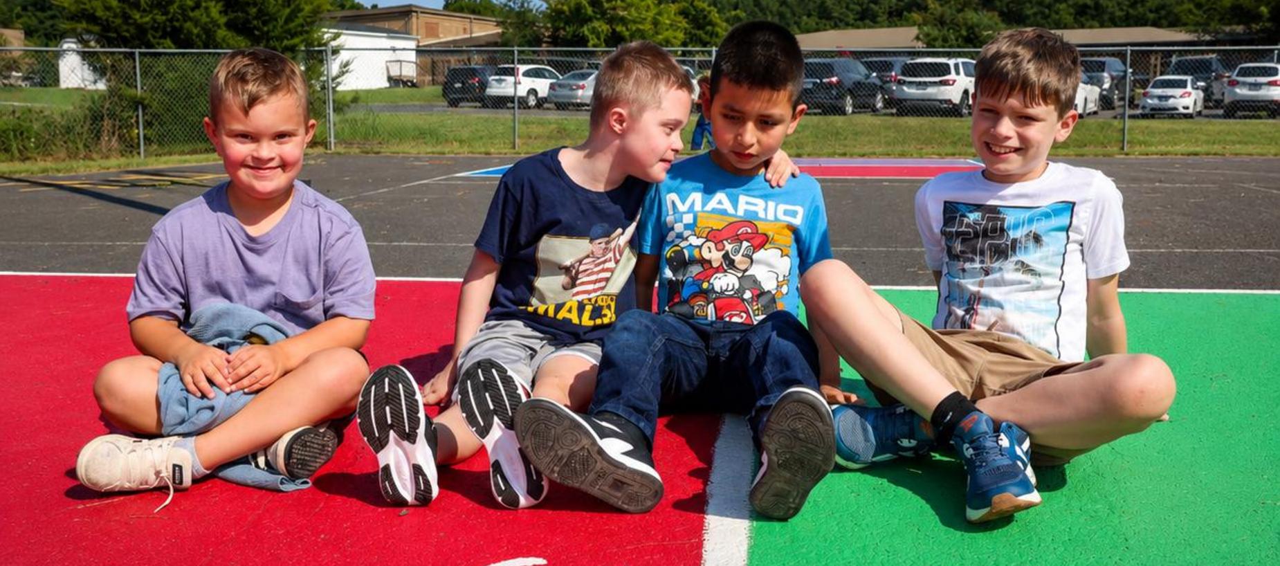 Four children sitting on a colorful playground court, smiling and relaxed.