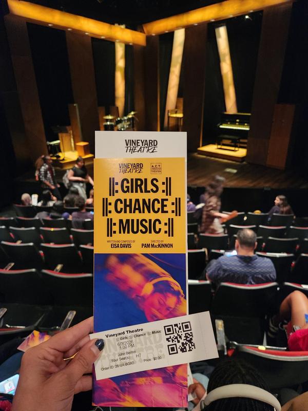 A hand holding a theatre program in front of an empty auditorium setting.