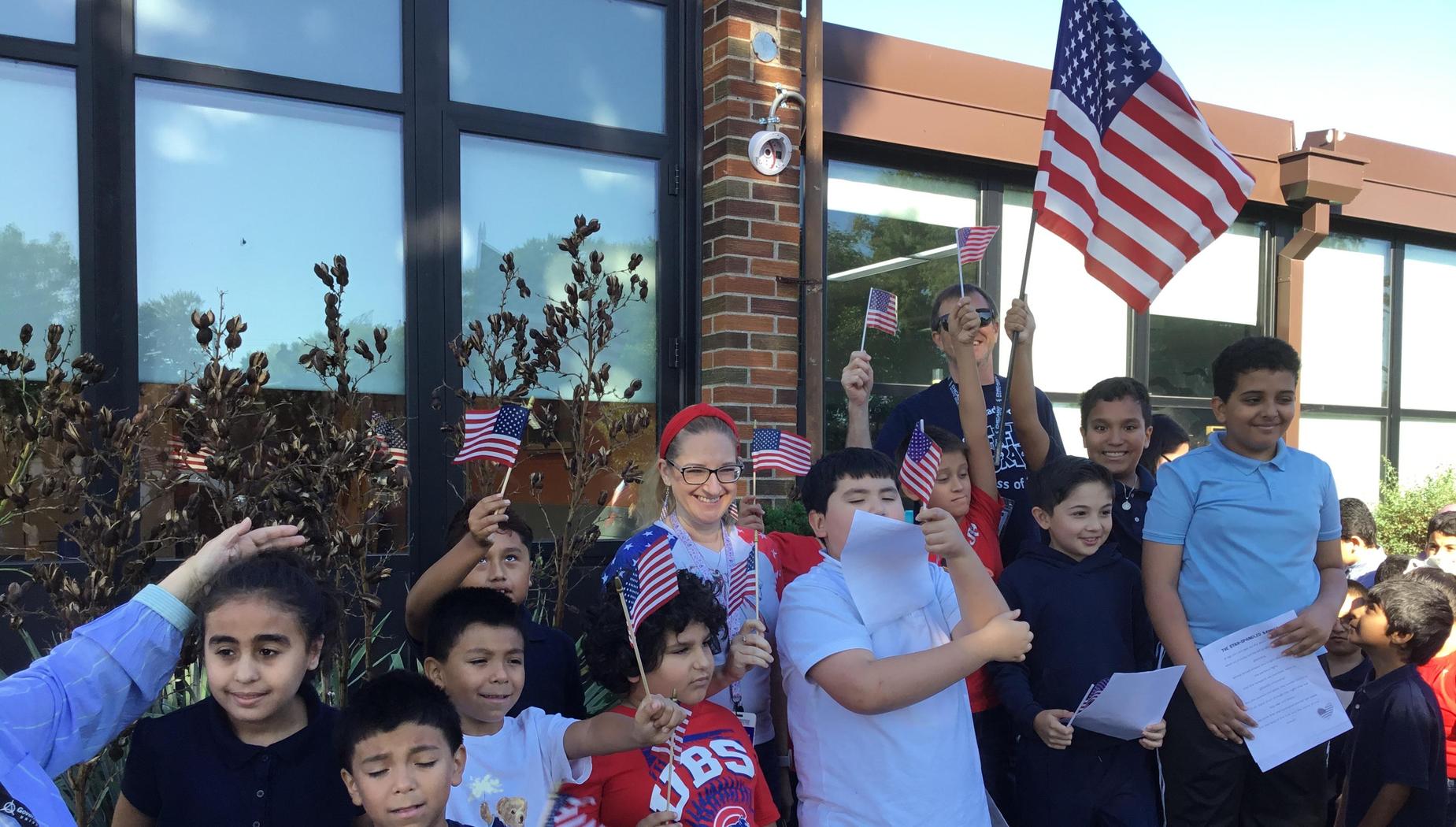 A group of children holding flags, celebrating outdoors near a building.