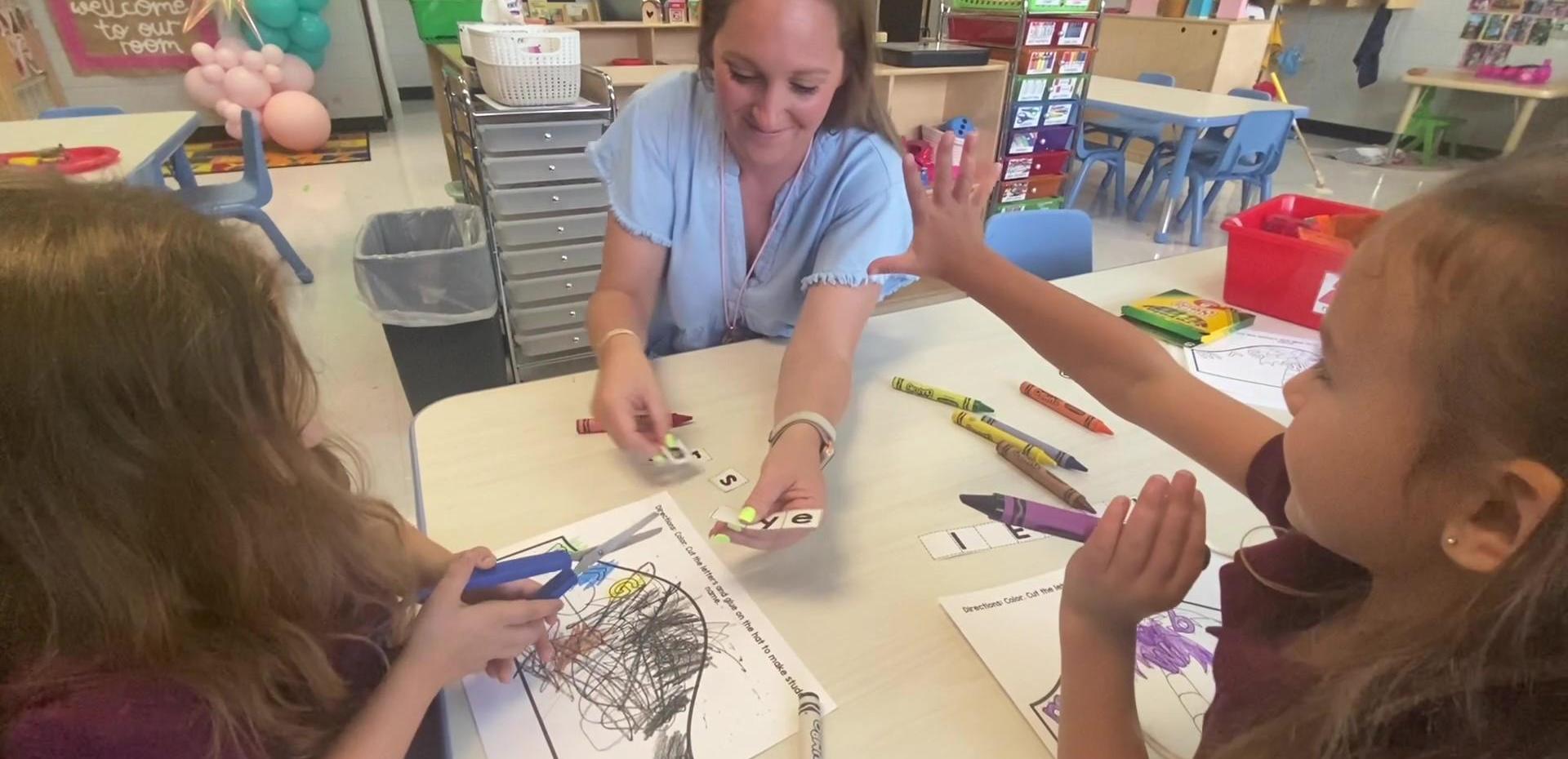 Teacher interacting with two girls at a table while working on art projects.