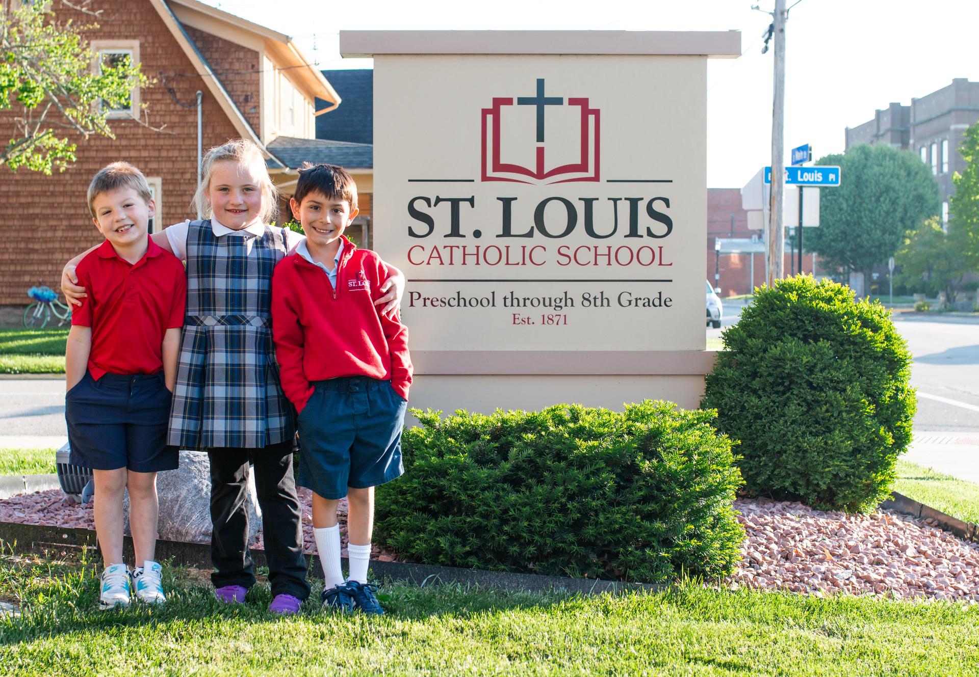 Students smiling standing in front of St. Louis School sign