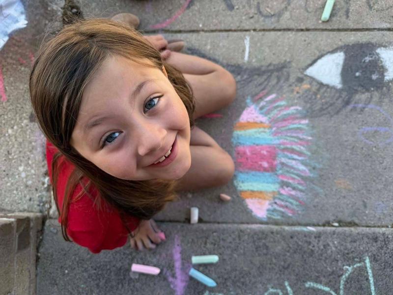 A girl sitting on the ground, smiling and surrounded by chalk art.