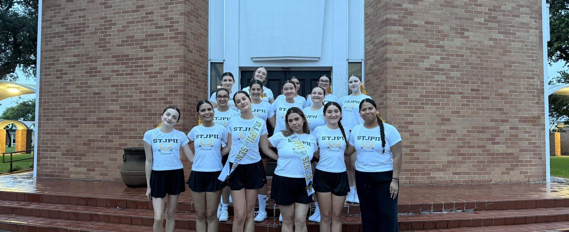 Group of cheerleaders posing together in front of a brick building.