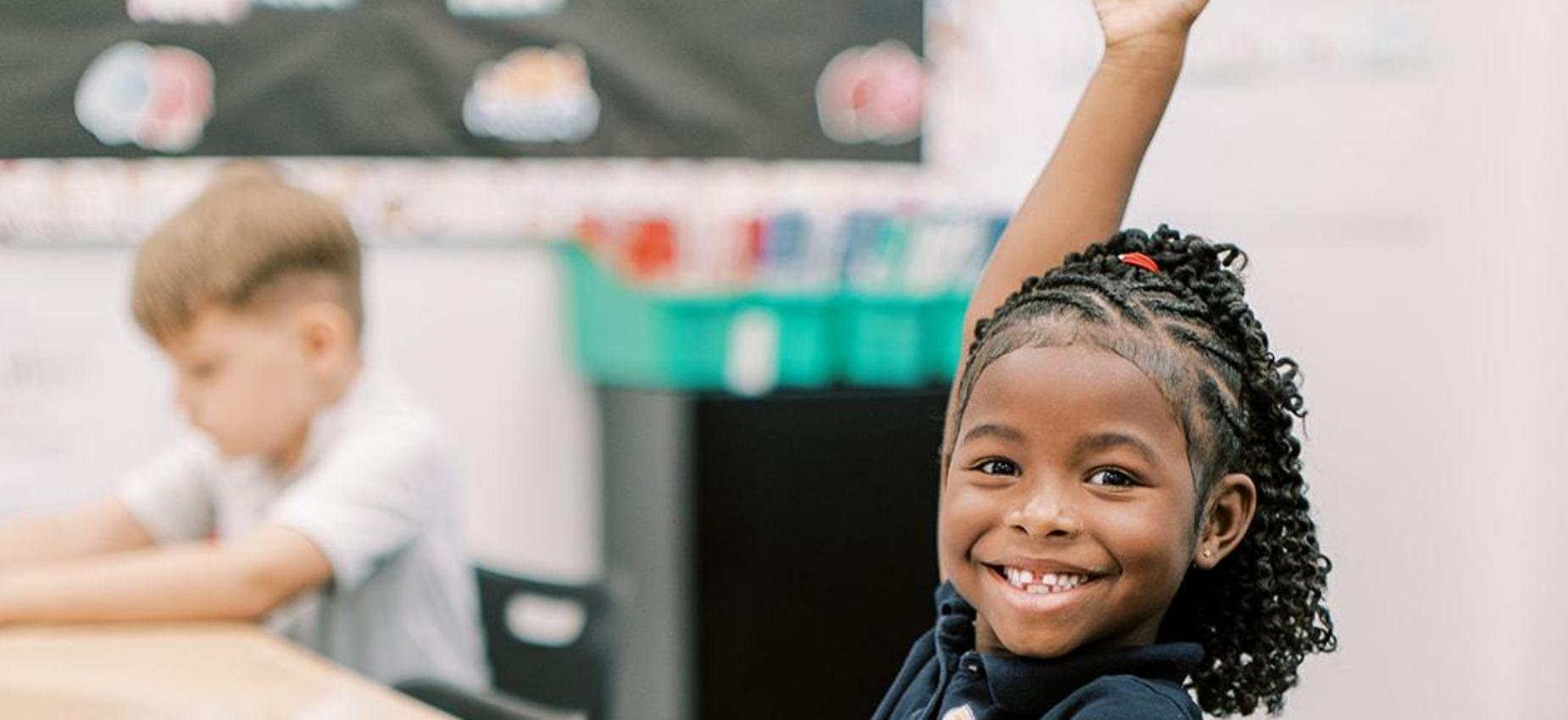 Smiling student raising her hand to answer a question in class