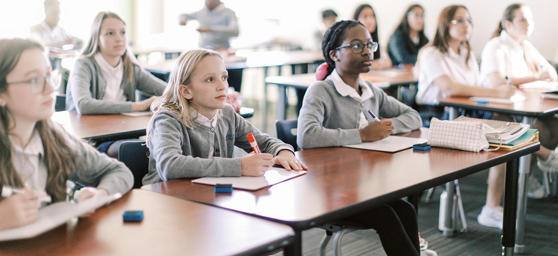 Elementary students write at their desks in a bright classroom