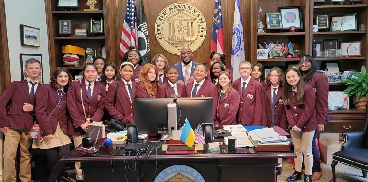 Students in blazers gathered around a desk in an office.