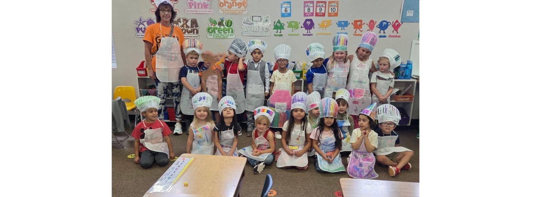 BES children wearing chef hats smiles together in a classroom.