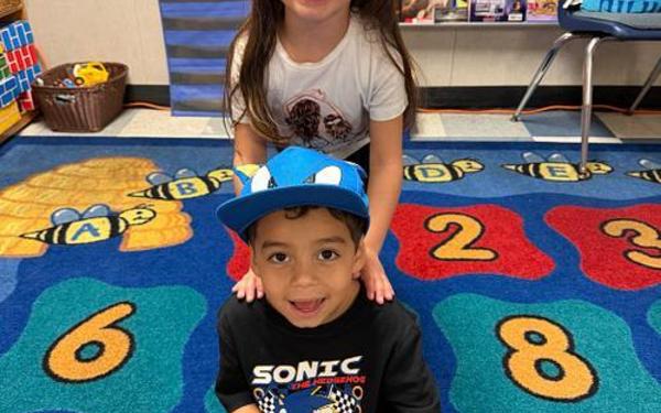Boy sitting crossed leg and girl standing behind him.