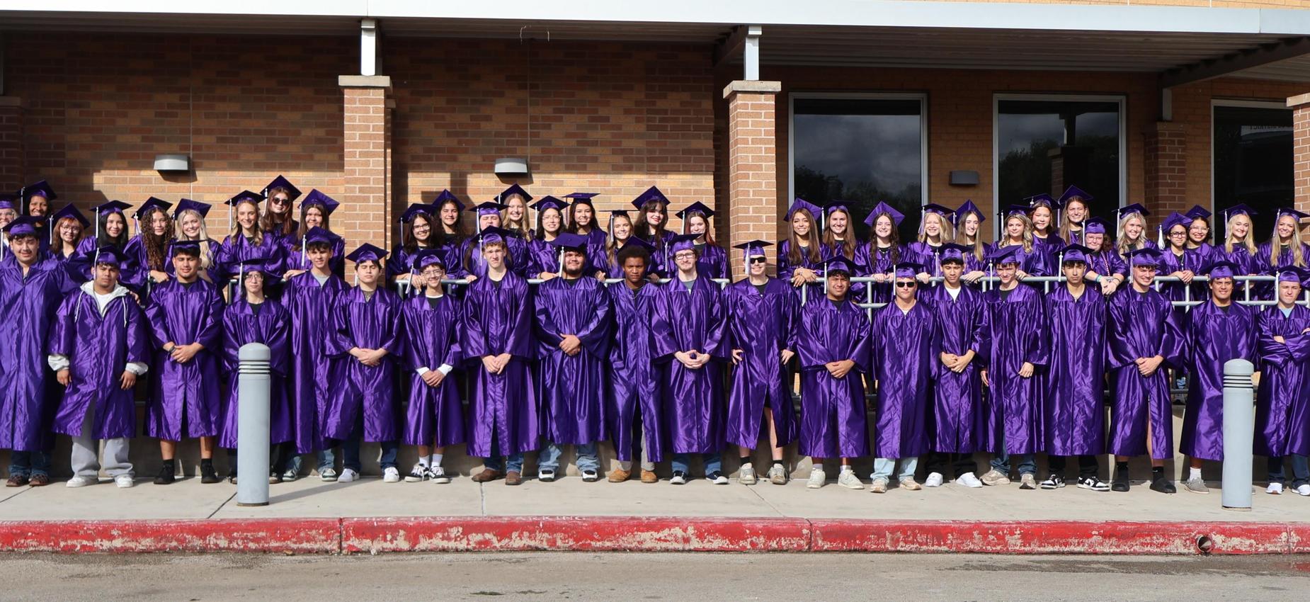 Senior Class of 2026 in their cap and gowns in front of the high school
