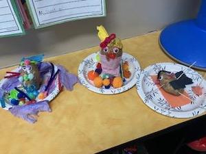 Three colorful craft projects on paper plates, displayed on a table.