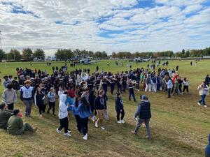 Image of students walking with the military band as they entertain the crowd
