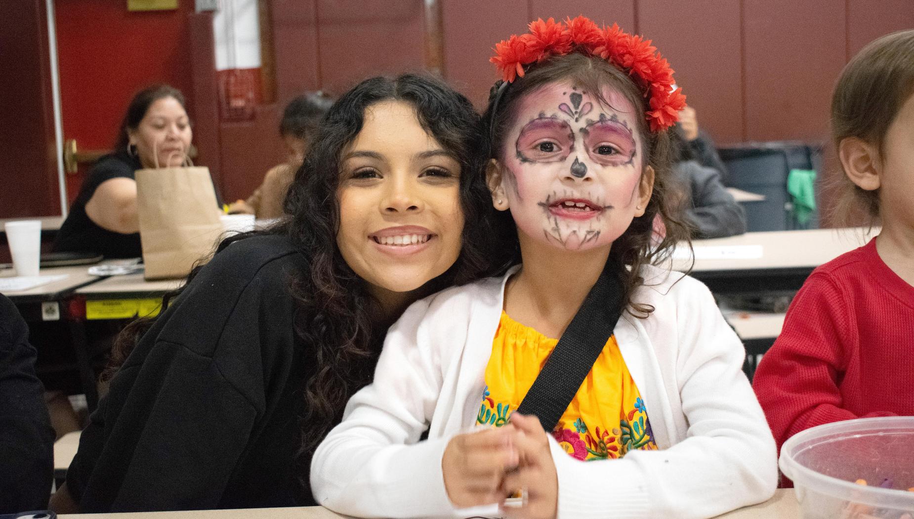 Young woman and a girl with colorful face paint, smiling together at a table.