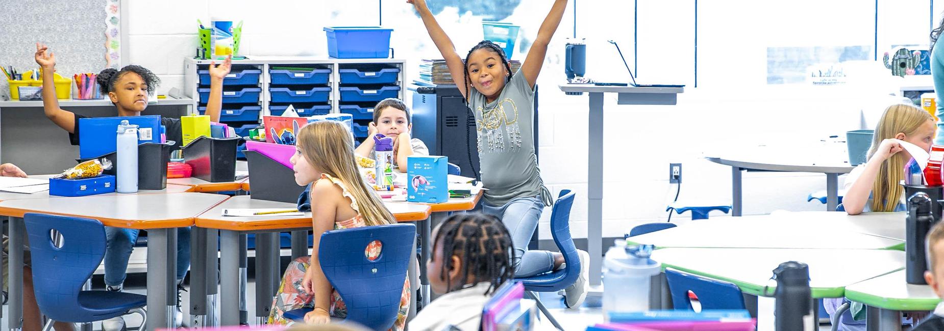 Students raising hands in a lively classroom setting.