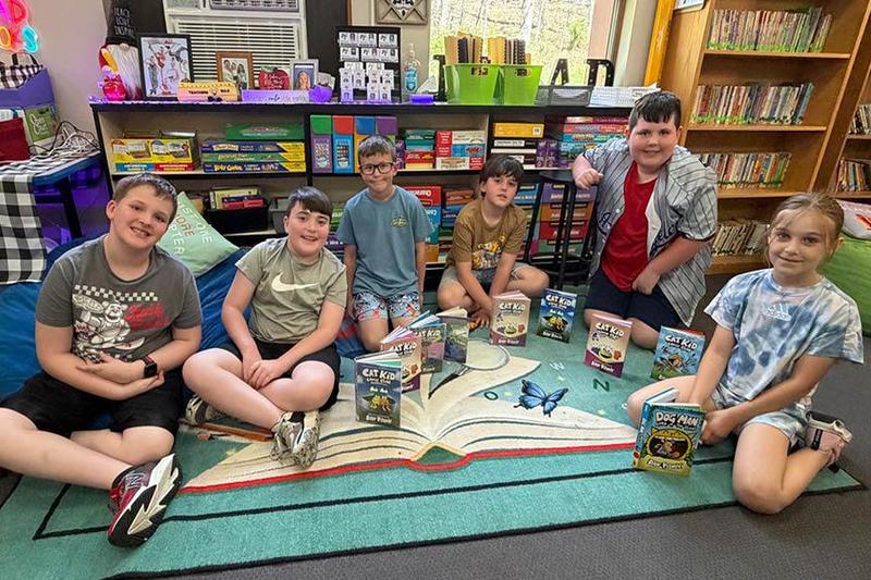 6 students are seated on the floor with many books sitting among them by the livestream authors