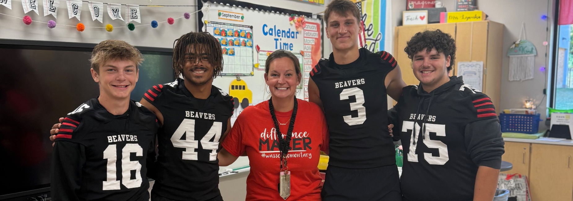 Group of four football players with a teacher in a colorful classroom.