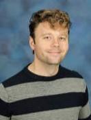 Blonde headed woman standing in front of a bush.