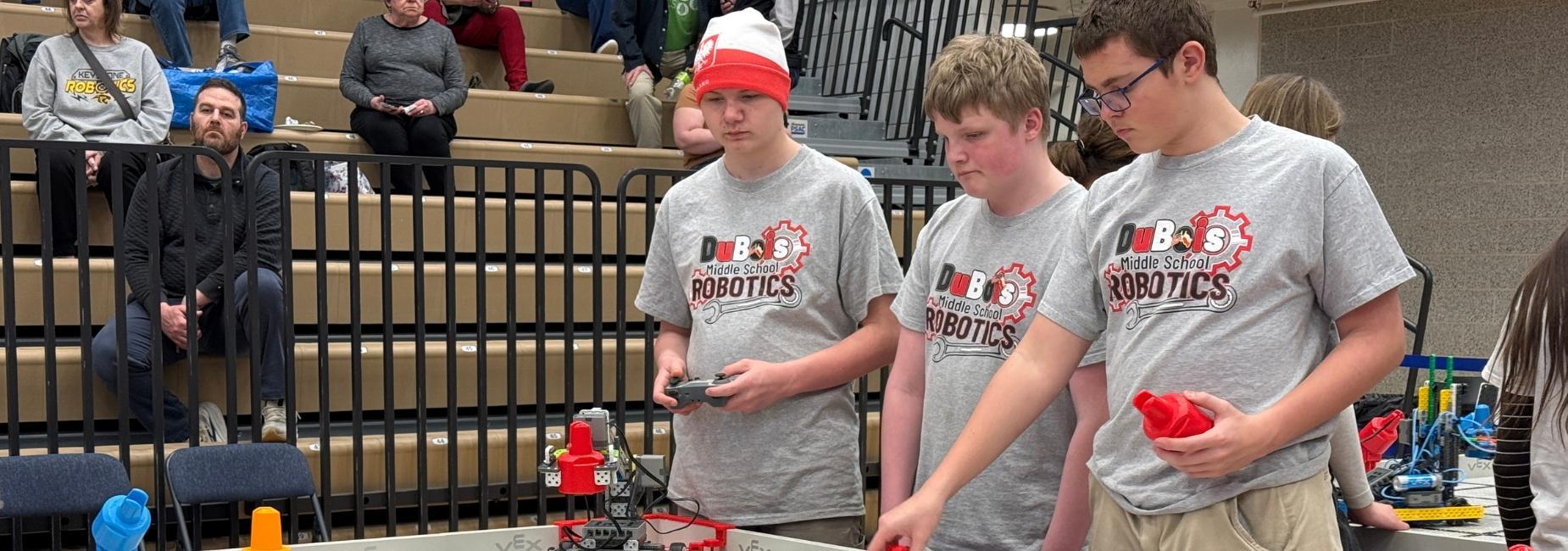 Three students working on a robotics project in a gym setting.