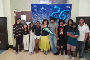 A group of nine people standing together in front of a celebratory backdrop.