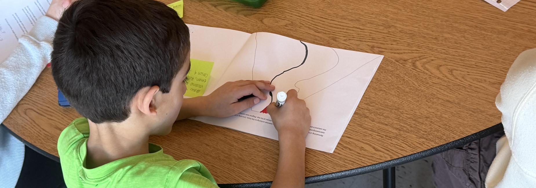 Child drawing on a sheet of paper at a table.