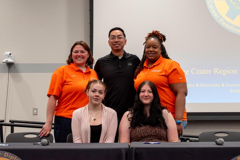 Two students smile with representatives from Super Radiator Coils during CTE Signing Day