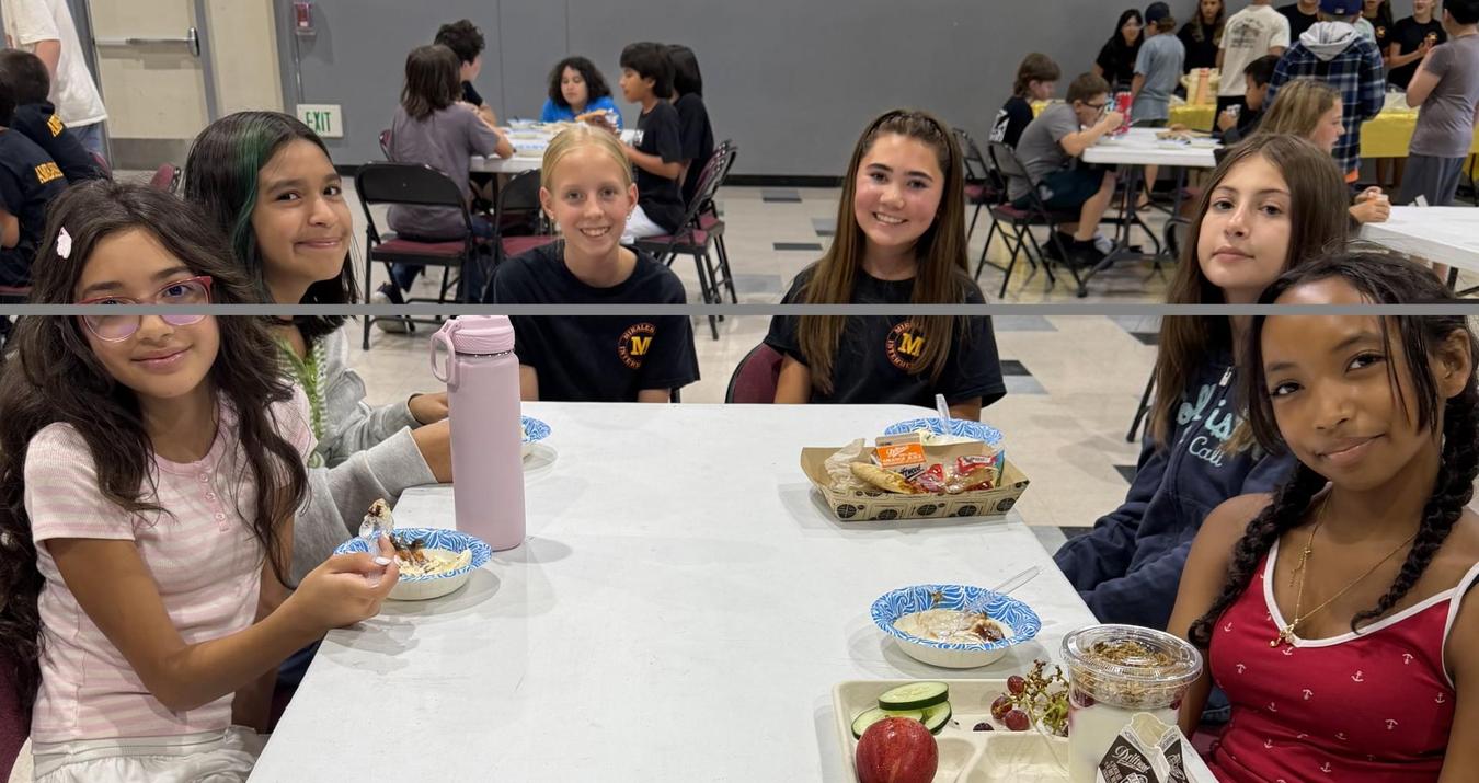 Children sitting at a table with snacks and drinks, engaging with each other.