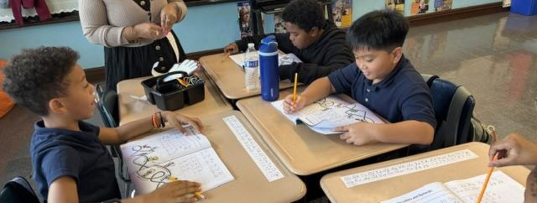 Students working on assignments at desks with books and supplies.